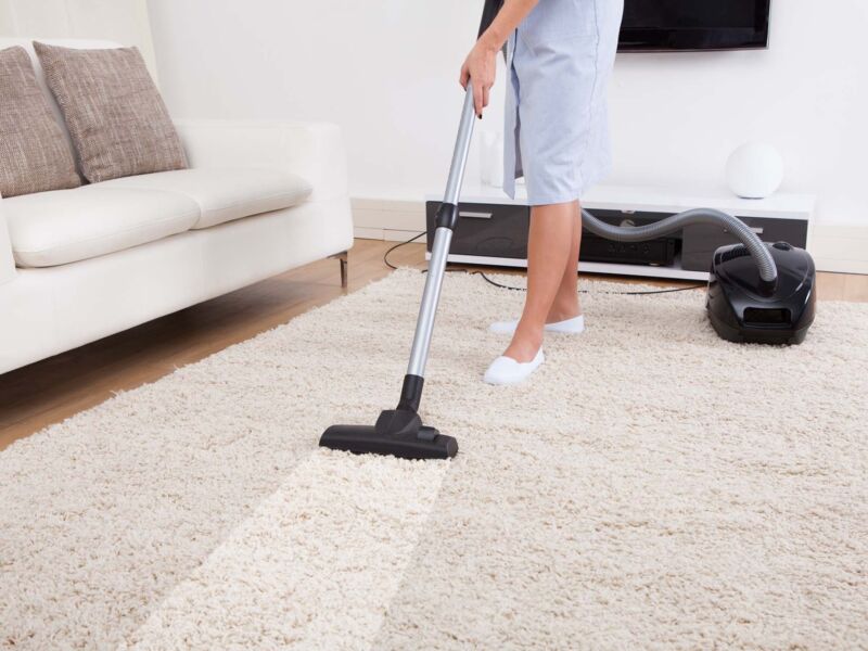 Cropped image of young maid cleaning carpet with vacuum cleaner at home
