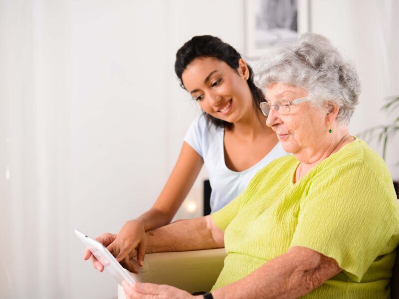 cheerful young girl with an elderly woman playing with digital tablet at home